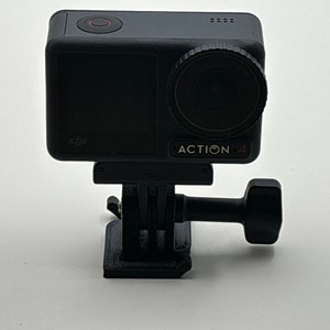 May include: A black DJI Action 4 camera with a black and silver lens and a red button on the top. The camera is mounted on a black tripod mount.