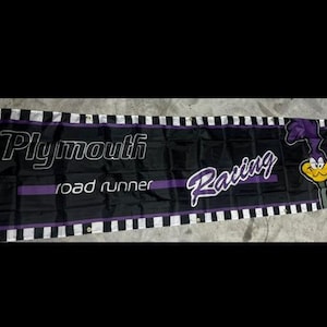 Pode incluir: Uma faixa xadrez preta e branca com o texto "Plymouth road runner racing" em branco e um roadrunner de desenho animado com penas roxas e bico amarelo.