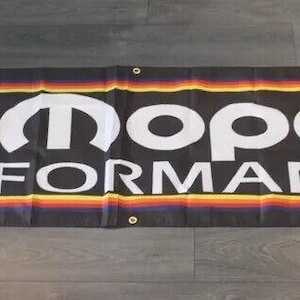 Pode incluir: Uma faixa preta com uma borda arco-íris e o texto "Mopar Performance" em letras brancas. O logotipo da Mopar é um M estilizado branco com uma estrela prateada dentro.