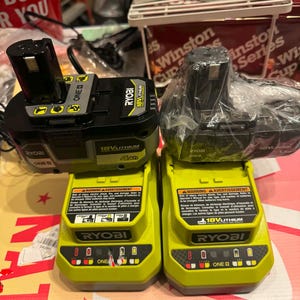 May include: Two Ryobi 18V lithium battery chargers in bright lime green and black. Each charger features a warning label, a battery slot, and LED indicator lights. One charger is paired with a 4Ah battery, while the other is wrapped in plastic.
