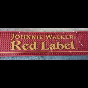 May include: A rectangular red bar mat with the words "JOHNNIE WALKER" and "Red Label" in gold lettering. The mat has a textured surface with small, raised circles.