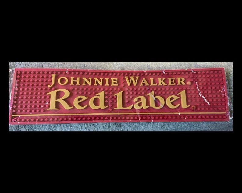 May include: A rectangular red bar mat with the words "JOHNNIE WALKER" and "Red Label" in gold lettering. The mat has a textured surface with small, raised circles.