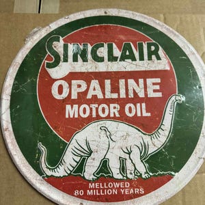 Puede incluir: Letrero redondo de Sinclair Opaline Motor Oil con un dinosaurio. El letrero tiene un fondo rojo y verde con texto blanco y una ilustración de dinosaurio blanco. El texto dice "Sinclair Opaline Motor Oil" y "Mellowed 80 Million Years".