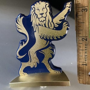 May include: A decorative lion figurine with a gold-colored lion design on a navy blue background. The lion is standing on its hind legs, with a gold-colored base. The figurine is approximately 2 inches tall.