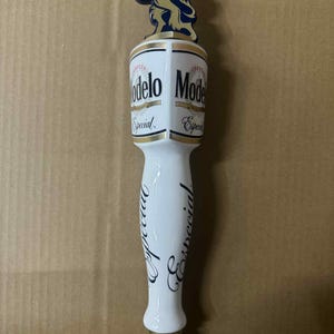 May include: A white and gold Modelo Especial beer tap handle. The handle features the Modelo Especial logo and a gold lion emblem. The handle is white with the word "Especial" written in a cursive font.