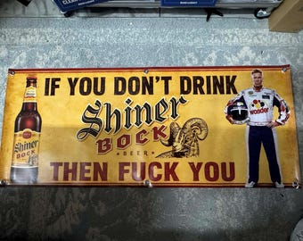 May include: A rectangular horizontal banner with a yellow background featuring a Shiner Bock beer bottle on the left, a ram illustration in the center, and a race car driver on the right. The text reads: IF YOU DON'T DRINK SHINER BOCK THEN FUCK YOU.