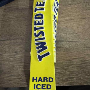 May include: A yellow Twisted Tea tap handle with blue lettering. The words "TWISTED TEA" are displayed vertically, with "HARD ICED TEA" below. The handle is rectangular and likely made of plastic, designed for a bar.
