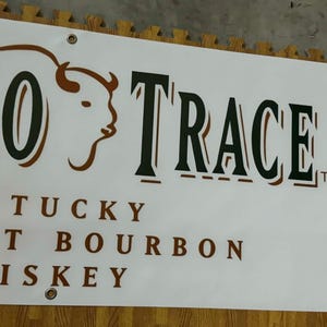 May include: White banner with the words "BUFFALO TRACE" in large, dark green letters with a brown buffalo head logo. Below, the text reads "KENTUCKY STRAIGHT BOURBON WHISKEY".