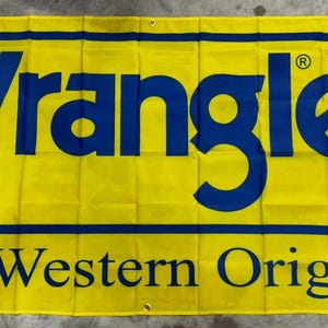 Może przedstawiać: Żółty baner z tekstem "Wrangler" w niebieskich literach i tekstem "The Western Original" w czarnych literach.