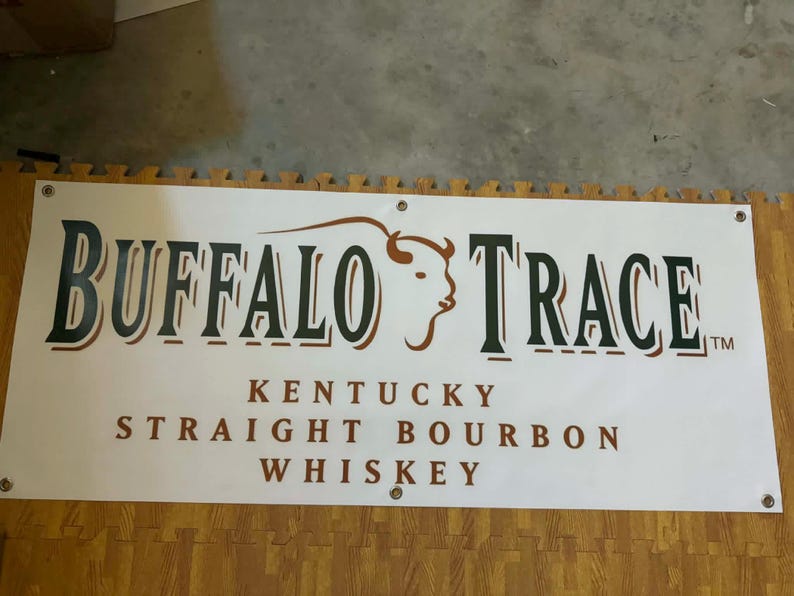 May include: A white banner with the words "BUFFALO TRACE" in large, dark green letters with a brown outline. Below, it reads "KENTUCKY STRAIGHT BOURBON WHISKEY" in brown. A bison graphic is featured.