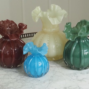 Op de afbeelding: Vier decoratieve glazen vazen in rood, geel, blauw en groen. Elke vaas heeft een gerimpelde bovenkant en een ronde body. De vazen zijn gerangschikt op een marmeren oppervlak.