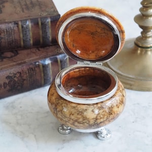 Può includere: Una tazza di ceramica bianca con manico nero e la scritta "But First, Coffee" in grassetto nero. La tazza è posta su uno sfondo sfocato, evidenziando il suo design semplice.