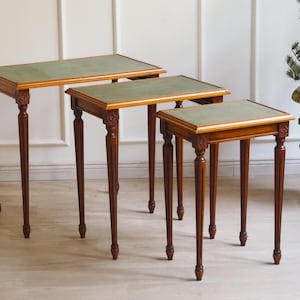 Könnte beinhalten: Satz von drei Beistelltischen mit rechteckigen grünen Tischplatten und dunkelbraunen Holzrahmen. Die Tische haben schlanke, geschnitzte Beine und dekorative Details. Der größte Tisch ist etwa 61 cm lang.