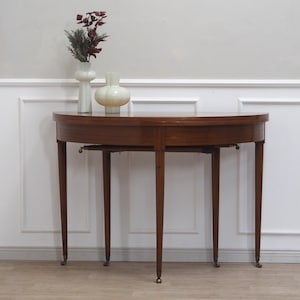 Könnte beinhalten: Ein brauner, halbrunden Holztisch mit vier Beinen. Der Tisch steht in einem Raum mit weißen Wänden und einer Täfelung.