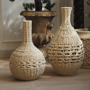 May include: Two woven beige vases with a textured design. One vase is smaller and more slender, while the other is larger with an open weave pattern. The vases are decorative and suitable for home decor.