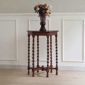 Könnte beinhalten: Ein antiker, dunkelbrauner Beistelltisch aus Holz mit quadratischer Platte und aufwendig gedrechselten Beinen. Eine Vase mit einem Blumenstrauß steht darauf. Der Tisch ist etwa 76 cm hoch.