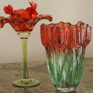 May include: Two glass decorative pieces. One is a tall, stemmed piece with a flared, orange top holding red objects. The other is a vase with a tulip-like design, transitioning from orange to green.