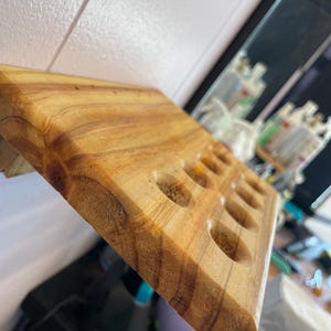 May include: A wooden, rectangular tray with multiple circular indentations. The tray is made of light brown wood with visible grain patterns. The design suggests it is for holding small items, possibly essential oils or small bottles.