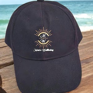 May include: Black baseball cap with a gold sunburst design and the letters "M" and "W" inside. The text "Men's Wellbeing" is written below the design.