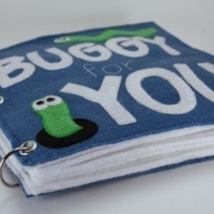 May include: A blue felt book with the words "Buggy for You" in white felt letters. The book has a green felt worm with googly eyes on the front cover and is bound with metal rings.