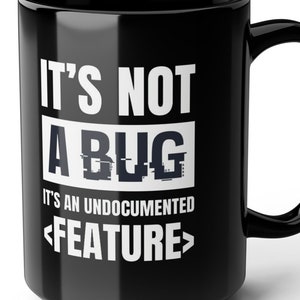 May include: Black ceramic mug with white text that reads "It's not a bug, it's an undocumented <feature>"