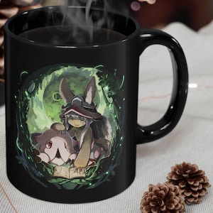 May include: Black ceramic mug with a white and green illustration of a girl with bunny ears and a red hat holding a small creature. The girl is reading a book.