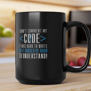 May include: Black ceramic coffee mug with a black handle. The mug features white and blue text that reads "I DON'T COMMENT MY <CODE> IT WAS HARD TO WRITE SO IT SHOULD BE HARD TO UNDERSTAND!"