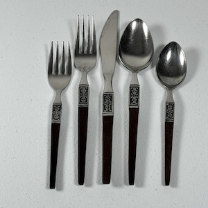 May include: A set of five pieces of silverware, including two forks, a knife, and two spoons. The silverware has dark brown handles with a decorative silver band near the top. The utensils are arranged in a row on a white surface.