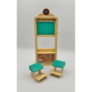 Peut inclure: Un ensemble scolaire en plastique beige comprenant une haute unité de tableau noir avec une horloge au sommet, une surface d'écriture verte et une étagère avec un graphique de bibliothèque imprimé. Deux pupitres assortis sont devant.
