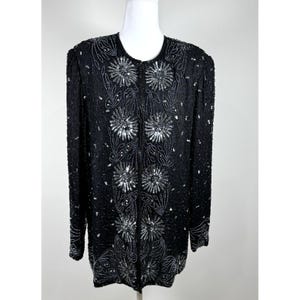 May include: A black beaded jacket with a round neck and long sleeves. The jacket has a floral design with silver sequins and beads. The jacket is fully beaded and has a zip closure.