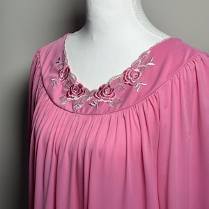 May include: A pink nightgown with a round neckline and embroidered rose detailing. The neckline is trimmed with a delicate lace. The fabric is gathered below the neckline, creating a flowing silhouette.