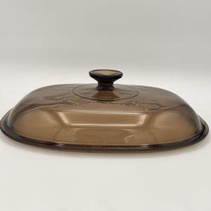Könnte beinhalten: Ovale, brauner Glasdeckel mit einem dunkelbraunen Knauf. Der Deckel ist leicht gewölbt und transparent. Er ist für Kochgeschirr konzipiert. Ein Küchenartikel.