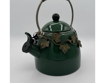 Tetera de metal verde vintage con decoración de hojas de vid, estilo rústico campestre.