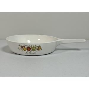 Puede incluir: Sartén de cerámica blanca con un mango largo. La sartén presenta una colorida ilustración de verduras y el texto "Le Persil" en el lateral. Un artículo de cocina.