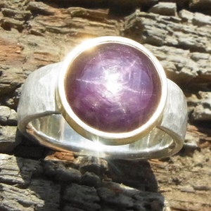 Peut inclure: Une bague en argent avec un sertissage en or et une grande pierre de saphir étoilé ronde et violette.