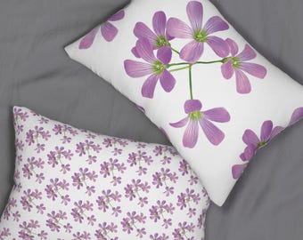 May include: Two decorative throw pillows. One pillow features a large floral design with purple flowers on a white background. The other pillow has a repeating pattern of smaller purple flowers on a white background. Both pillows are rectangular.