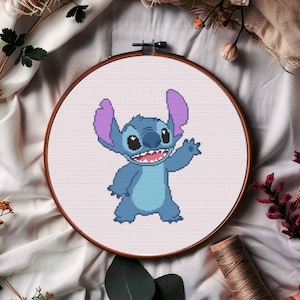 Puede incluir: Un patrón de punto de cruz con el personaje Stitch, de color azul y morado, en un aro de bordado de madera. El personaje sonríe y saluda.