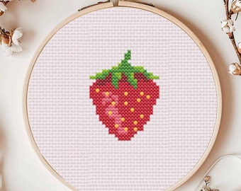 May include: A cross-stitch embroidery of a red strawberry with green leaves and yellow seeds, set in a wooden embroidery hoop. The strawberry design is centered on a light pink fabric background.