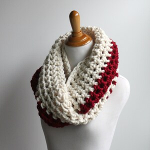 May include: A white and burgundy crocheted infinity scarf. The scarf is made with a chunky yarn and has a simple, textured stitch.