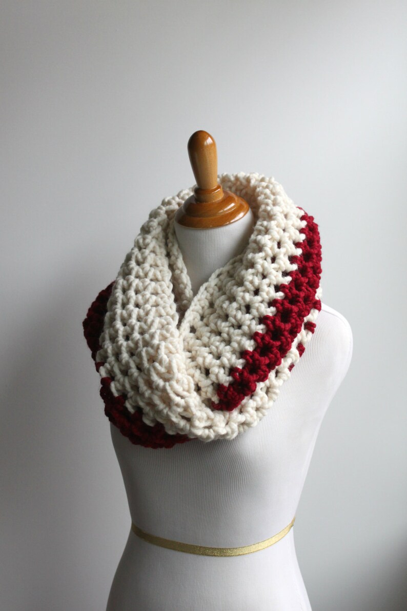 May include: A white and burgundy crocheted infinity scarf. The scarf is made with a chunky yarn and has a simple, textured stitch.