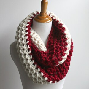 May include: A white and burgundy crocheted infinity scarf. The scarf is made with a chunky yarn and has a simple, textured stitch.