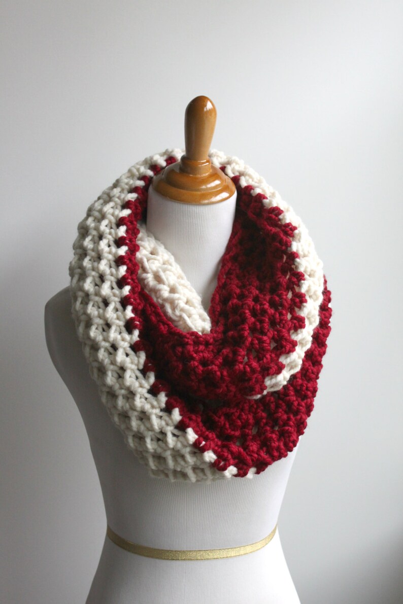 May include: A white and burgundy crocheted infinity scarf. The scarf is made with a chunky yarn and has a simple, textured stitch.