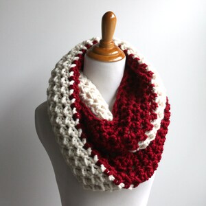 May include: A white and burgundy crocheted infinity scarf. The scarf is made with a chunky yarn and has a textured stitch.