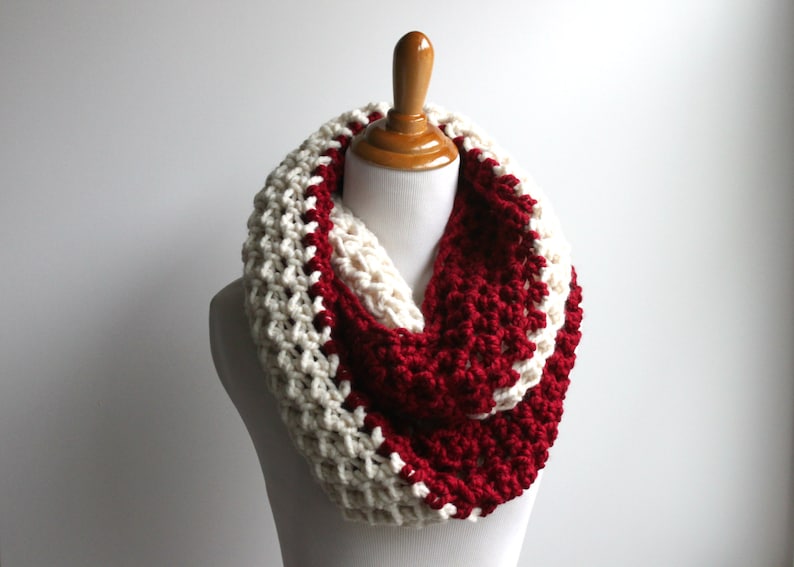 May include: A white and burgundy crocheted infinity scarf. The scarf is made with a chunky yarn and has a textured stitch.