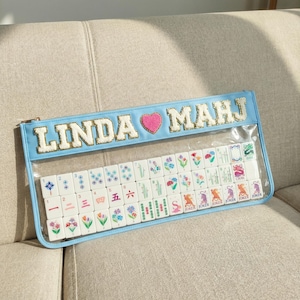 May include: A white ceramic mug with a black handle and the text "But First, Coffee" in a black, handwritten-style font. The mug is on a white surface.