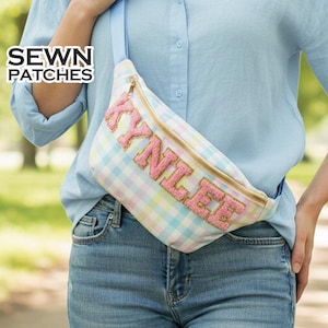 May include: A pastel plaid fanny pack with the name "KYNLEE" in pink embroidered letters. The bag has a gold zipper and a light blue strap. The text "SEWN PATCHES" is in the upper left corner.