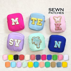 Könnte beinhalten: Ein Set aus sechs kleinen, quadratischen Stoffbeuteln mit verschiedenen Stofffarben und gestickten Designs. Die Beutel sind rosa, hellblau, lavendel, hellgrün, blau und rosa. Die Designs beinhalten Buchstaben, eine Palme und einen Schmetterling. Die Beutel sind mit "SEWN PATCHES" beschriftet.