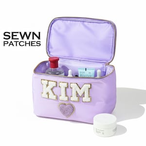May include: A lavender cosmetic bag with the name "KIM" in white and gold letters, and a purple heart. The bag is open, revealing various cosmetic products. The text "SEWN PATCHES" is in the upper left corner.