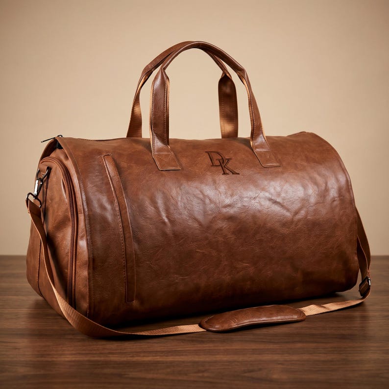 Puede incluir: Una bolsa de viaje marr&oacute;n con acabado texturizado, que cuenta con dos asas superiores y una correa de hombro extra&iacute;ble con una secci&oacute;n acolchada. La bolsa tiene un compartimento lateral con cremallera y las letras DK grabadas en el frente.