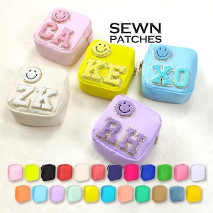 Könnte beinhalten: Ein Set mit 25 bunten, kleinen, quadratischen Reißverschlusstaschen mit einem Smiley-Gesicht und gestickten Buchstaben. Die Taschen sind in verschiedenen Farben erhältlich, darunter Gelb, Blau, Grün, Rot, Pink und Weiß. SEWN PATCHES steht in schwarzer Schrift oben im Bild.